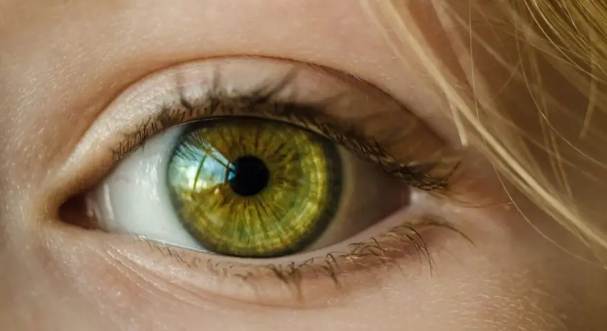 Zielona soczewka oka z refleksami światła, otoczona jasną skórą i blond włosami.