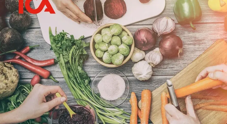 ICA-logotypen över en bild av färska grönsaker som förbereds för ett recept. Rödbetor skivas, morötter skalas och en skål med puré.