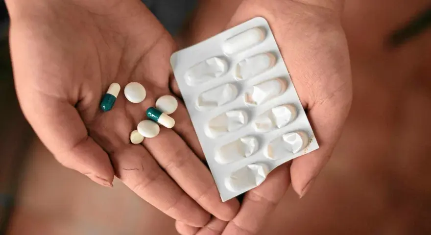 Dłonie trzymające tabletki i blister. Wśród nich są leki, które mogą być inhibitorami pompy protonowej, pomagając w leczeniu dolegliwości żołądkowych.