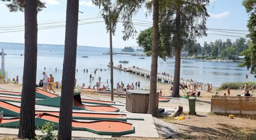 Minigolfbana vid Engesbergs camping. Många badar och solar vid vattnet, en brygga leder ut i sjön.