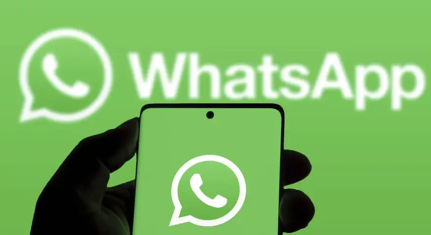 Hand hält Smartphone mit WhatsApp-Logo vor grünem Hintergrund.