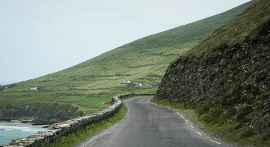 A winding road along the coast of Ireland, perfect for renting a car and exploring the dramatic green hills and stone walls.