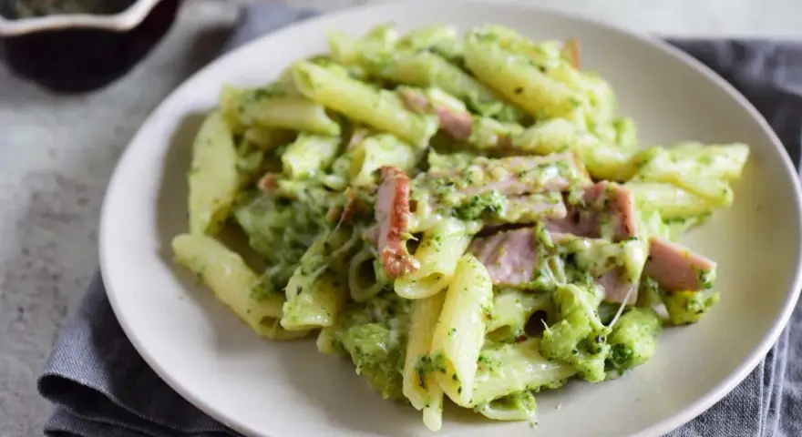 Penne z brokułami i kawałkami szynki w kremowym sosie śmietanowym, posypane serem. Pyszne danie, które zachwyci każdego.