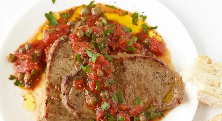 Zwei saftige Scheiben Rindfleisch, bedeckt mit einer würzigen Tomaten-Kapern-Sauce, serviert mit Brot. Ein authentisches Gericht im Stil Pizzaiola original italienisch.