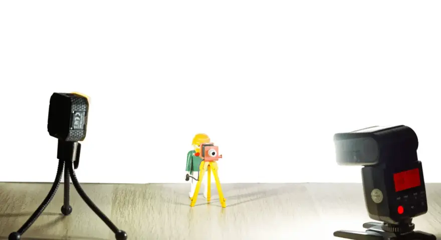 Une figurine Playmobil prend une photo avec un appareil sur trépied. Une autre caméra et un flash sont présents. Vue macro.
