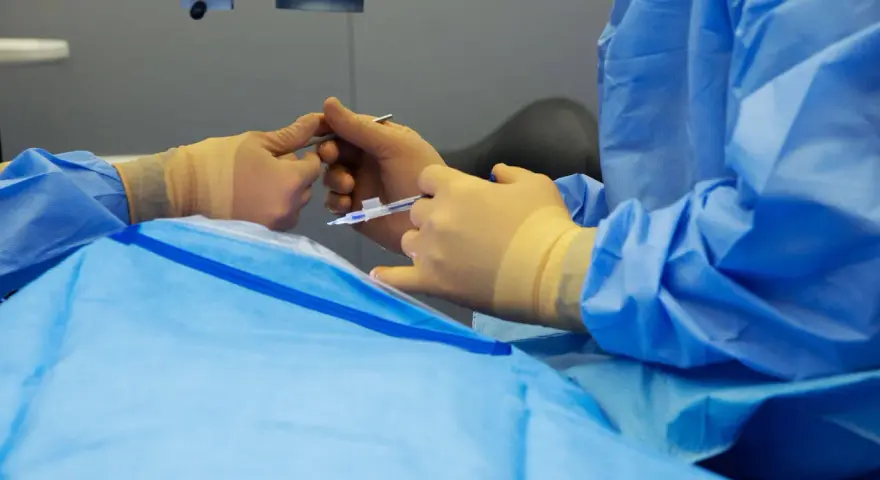 Mani guantate eseguono un intervento chirurgico oculare, forse un piombaggio retina, con precisione.
