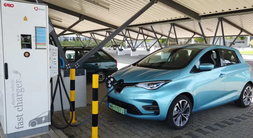 Błękitny Renault Zoe podłączony do ładowarki na parkingu pod zadaszeniem.