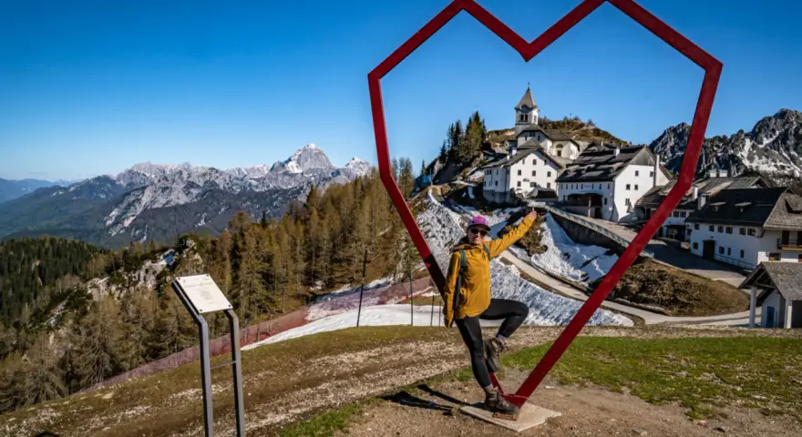 Kobieta w sercu z widokiem na górską wioskę Monte Lussari.