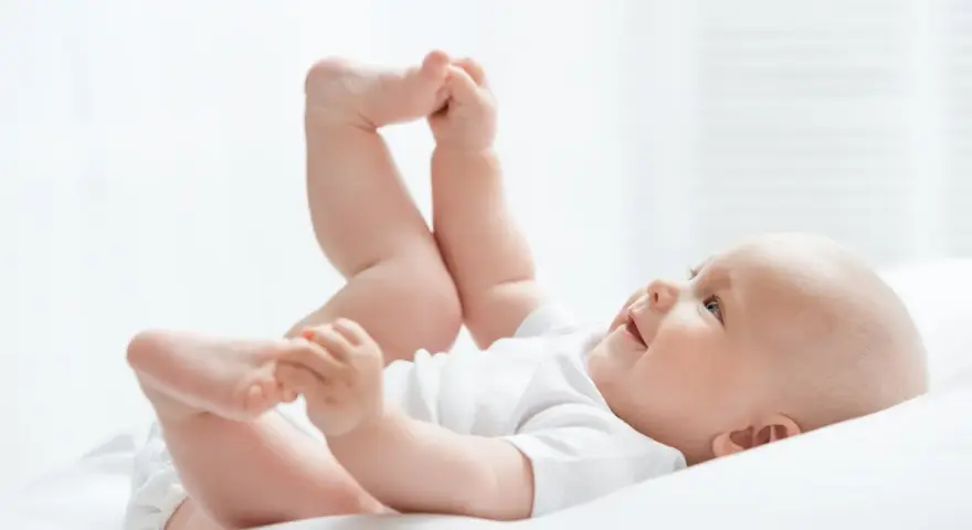 Uśmiechnięte dziecko leży na plecach, podnosząc nóżki. Czas na zmianę pampersów na większe, gdy maluch rośnie.