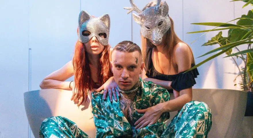 Smolasty z dużymi oczami w otoczeniu dwóch kobiet w błyszczących maskach.