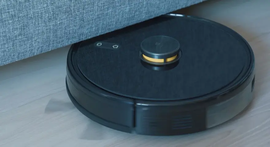 En robotdammsugare navigerar under en soffa, visar hur fungerar en robotdammsugare.