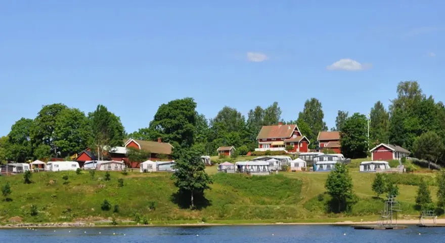 Gröna kullar med husbilar och röda stugor vid en sjö. En idyllisk plats för greans camping.