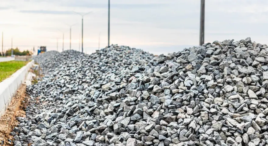 Stos kruszywa, idealnego jako składnik betonu B25, na tle słupów oświetleniowych i nieba.