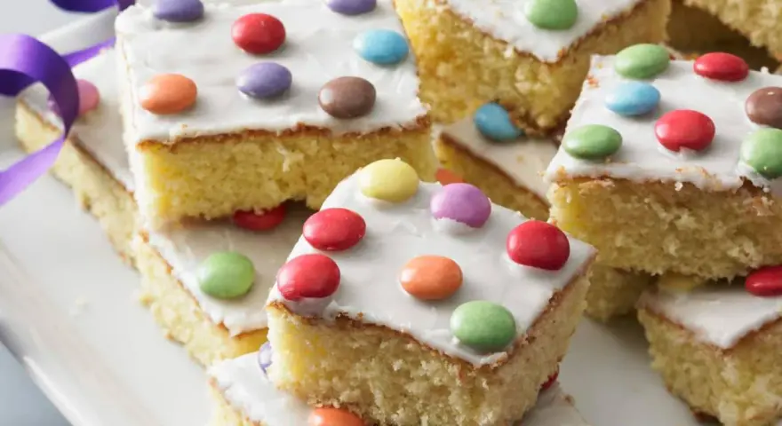 Bunter Fantakuchen-Rezept: saftige Kuchenstücke mit weißer Glasur und bunten Smarties. Perfekt für Kindergeburtstage!