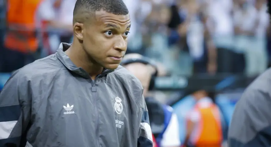 Kylian Mbappé w szarej kurtce z logo Realu Madryt, gotowy do gry.