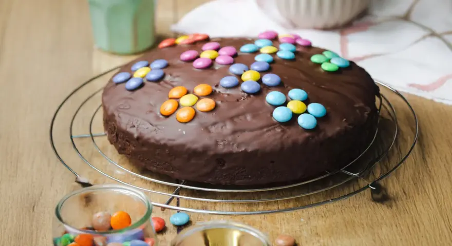 Schokokuchen mit bunten Smarties, perfekt für Kinder. Ein Glas mit weiteren Süßigkeiten steht daneben.