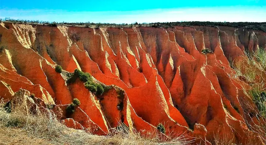 Impresionantes cárcavas en España, con formaciones rojizas y vegetación escasa bajo un cielo azul intenso.