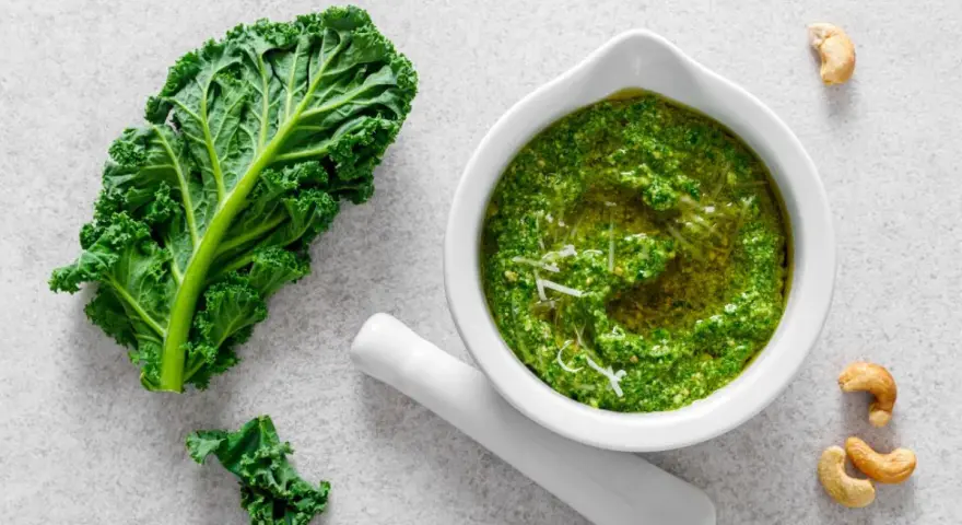 Pesto z jarmużu do słoika, gotowe do przechowywania. Obok liść jarmużu i orzechy nerkowca.