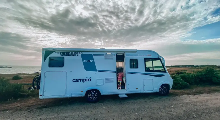 Kamper na wybrzeżu Szwecji, gotowy na przygodę. Dziecko w drzwiach, chmury na niebie. #szwecja kamperem