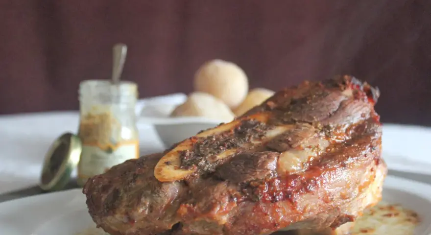 Costilla de ternera asada jugosa con hueso, servida en plato blanco con salsa y guarnición.