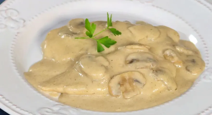 Pollo cremoso con champiñones y perejil en un plato blanco.