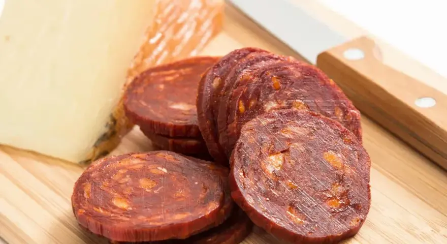Plasterki pikantnego chorizo, kawałek sera i nóż na desce. Idealne na przekąskę, zastanawiasz się chorizo co to?