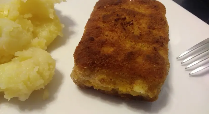 Chrupiąca panierowana kostka rybna z purée ziemniaczanym na białym talerzu.