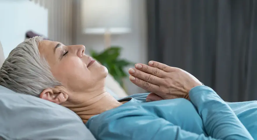 Frau liegt entspannt im Bett, Hände vor der Brust gefaltet. Sie praktiziert eine Technik, die wirkt Meditation im Schlaf.