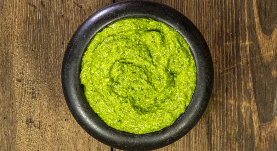 Pesto genovese ricetta originale in un mortaio di pietra, su un tavolo di legno rustico. Fresco e profumato.