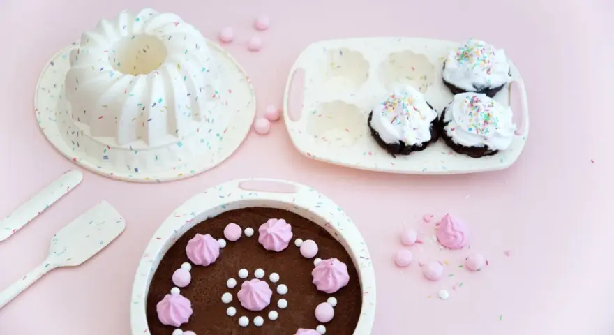 Förberedelser för ett härligt baka kalas! En sockerkaksform, muffinsform och en färdig chokladkaka med rosa maränger och strössel.