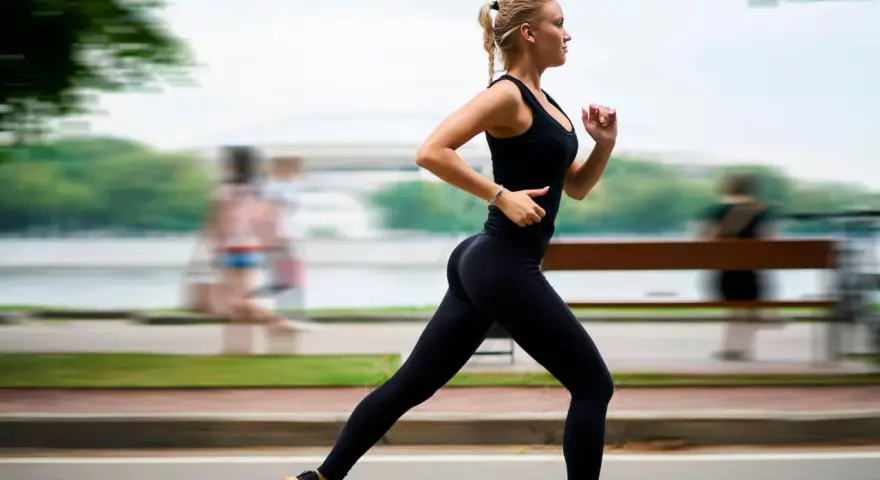 Donna bionda in abbigliamento sportivo nero corre con una postura corsa perfetta lungo un percorso alberato.