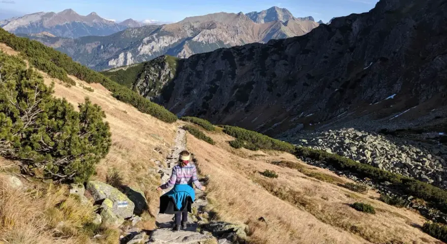 Osoba wędruje kamienistym szlakiem w Tatrach. Widok na góry i dolinę, idealne tatry szlaki dla średnio zaawansowanych.