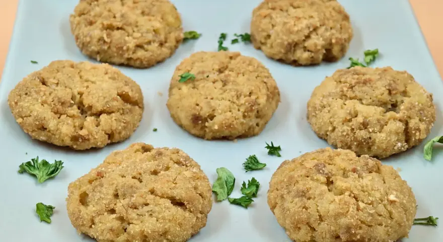 Sei polpette di patate dorate e croccanti, guarnite con prezzemolo fresco, su un piatto azzurro.