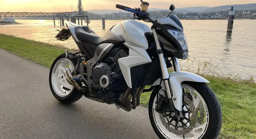 Biały motocykl Honda z silnikiem 35 kw nad rzeką o zachodzie słońca.