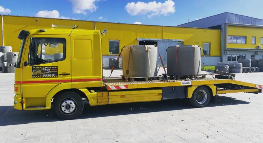 Żółta laweta z dwoma betonowymi elementami, gotowa do transportu. To **assistance warta** uwagi, gdy potrzebujesz przewieźć ciężkie ładunki.