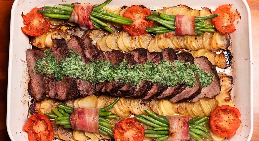 En saftig coeur de filet provencale med potatis, gröna bönor inslagna i bacon och tomater i en ugnsform.