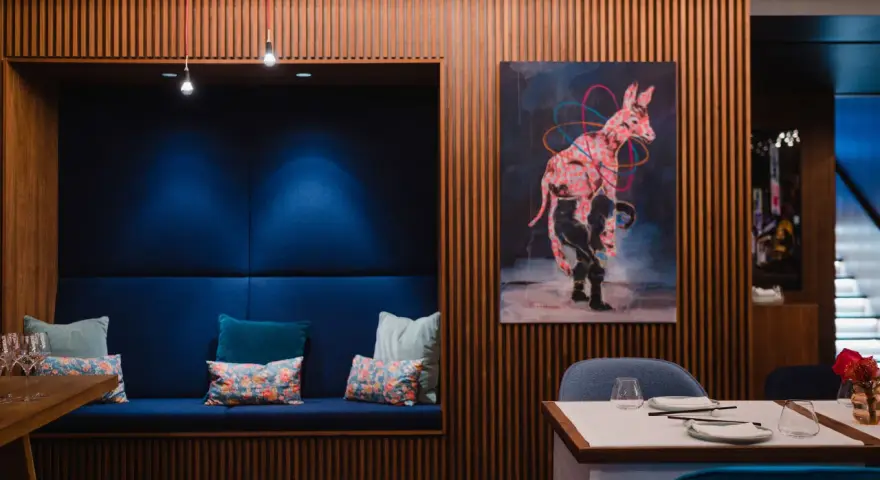 Gemütliche Nische mit blauen Kissen und einem orientalischen Teppich. Ein Kunstwerk mit einem pinken Zebra ziert die Holzwand. Ein echter Berlin Restaurant Geheimtipp.