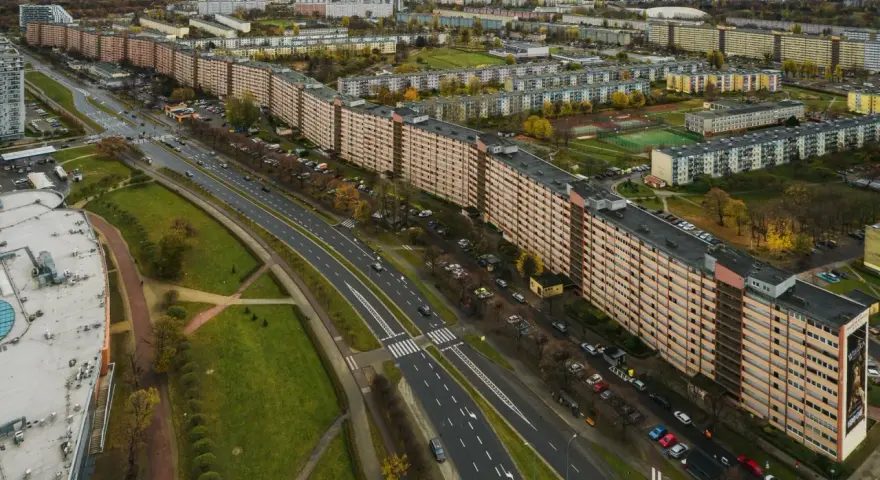 Widok z lotu ptaka na najdłuższy blok w Europie, rozciągający się wzdłuż ruchliwej drogi i otoczony zielenią oraz innymi budynkami mieszkalnymi.