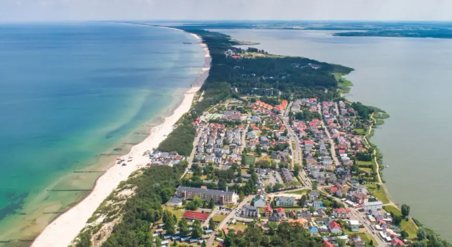 Widok z lotu ptaka na Mielno: plaża, morze, jezioro i zabudowania.