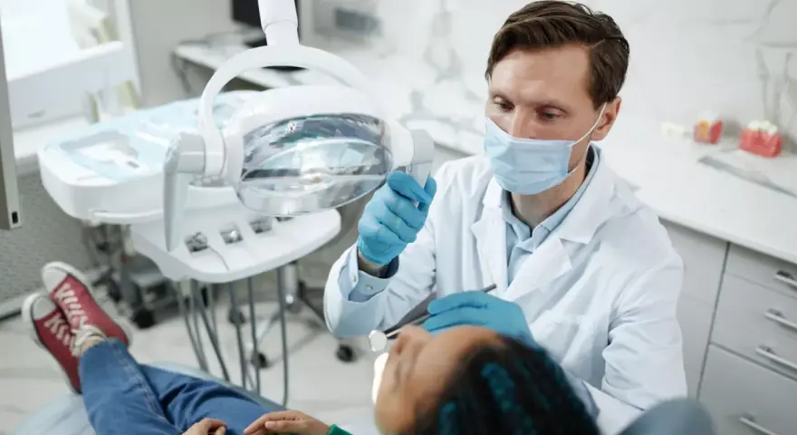 Dentysta w masce i rękawiczkach bada pacjenta w gabinecie stomatologicznym.