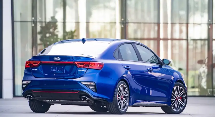 Niebieski sedan Kia Forte z widokiem z tyłu, z czerwonymi akcentami i sportowymi felgami.