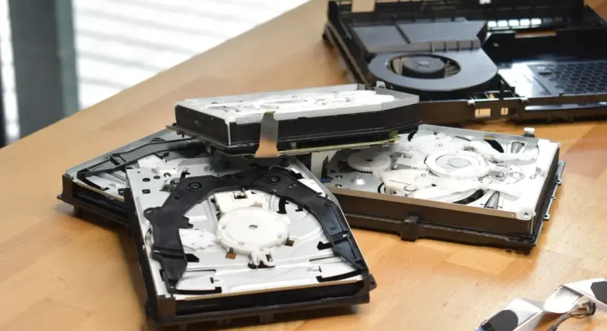 Rozłożone wnętrze konsoli PS4 Slim, widać dysk i mechanizm napędu. Komponenty leżą na drewnianym blacie, przypominając o kompaktowych ps4 slim wymiary.