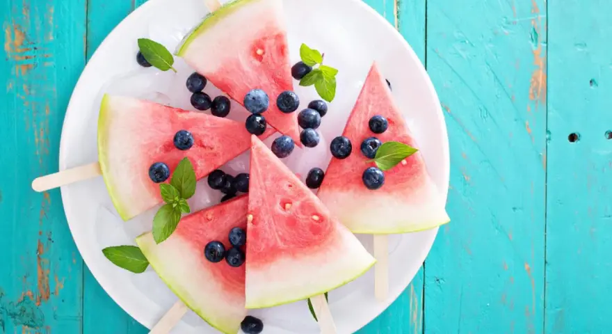Erfrischendes Wassermelonen Eis mit Blaubeeren und Minze auf Eiswürfeln, serviert auf einem weißen Teller.