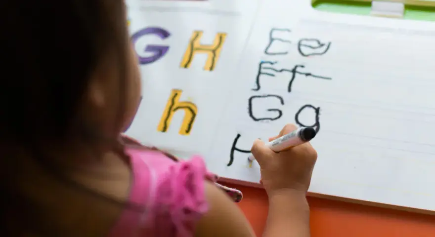 Dziecko ćwiczy łączenie liter pisanych na tablicy. Litery G, H, h, E, F, G, H.