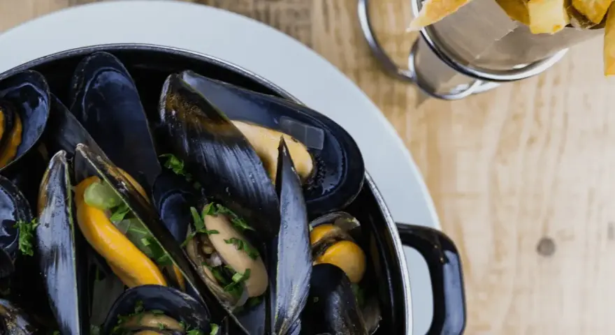 En stor kastrull med ångande blåmusslor, perfekt för en måltid med vin till moules frites. Pommes frites syns i bakgrunden.