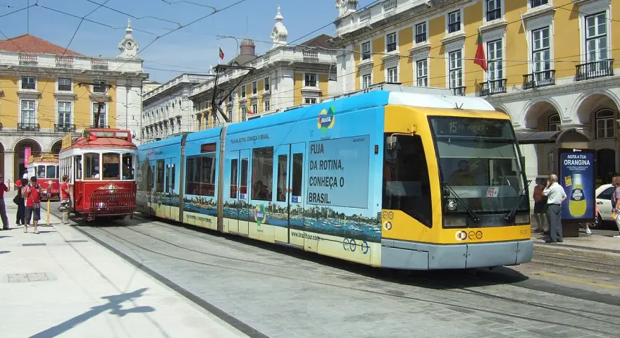 Lizbona tramwaj: nowoczesny, niebiesko-żółty pojazd obok zabytkowego, czerwonego tramwaju na tle żółtych budynków.