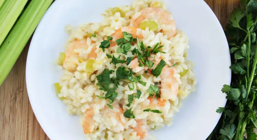Pyszne risotto z krewetkami, ozdobione natką pietruszki, obok łodygi selera i oliwy.