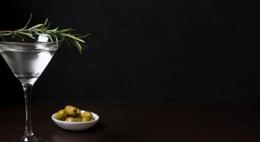 Elegancki kieliszek z drinkiem, gałązka rozmarynu i oliwki. Czy to Dirty Martini, czy klasyczne Dry Martini?