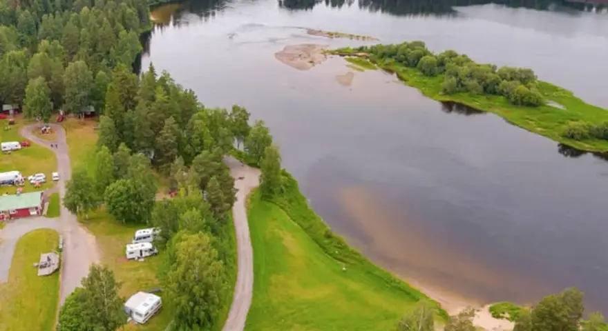 Vacker vy över Selholmens camping med husbilar och stugor vid en sjö omgiven av skog.