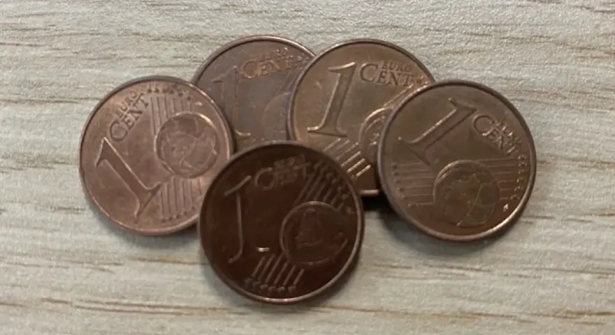 Cinq pièces de 1 centime d'euro, certaines semblant être une pièce de 1 euro rare valeur, sont disposées sur une surface en bois.
